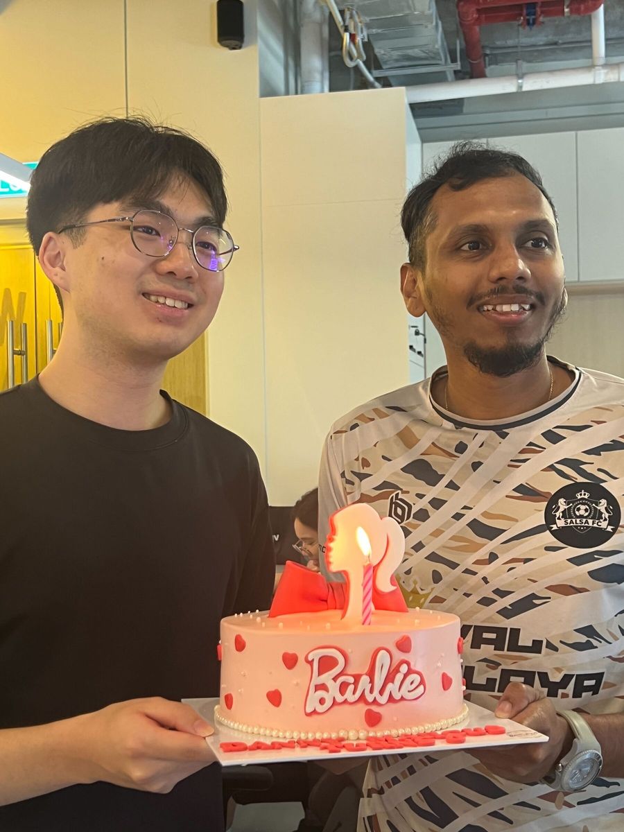 Two teammates smiling with a Barbie-themed birthday cake in the office