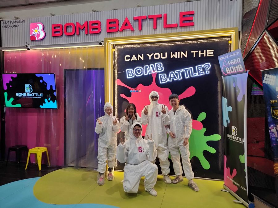 Teammates in white paint suits posing in front of the Bomb Battle game arena