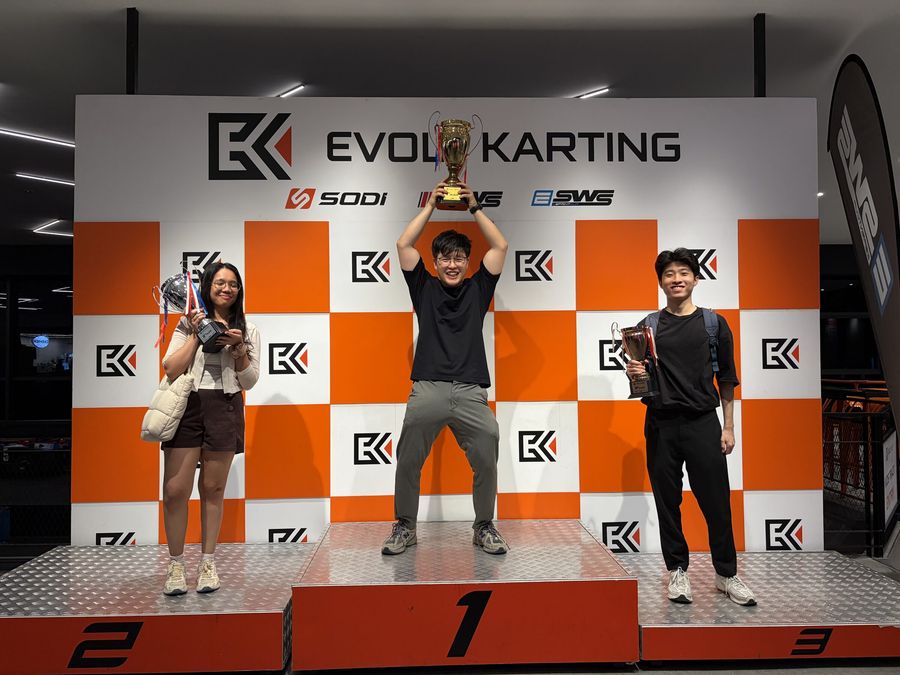 Three teammates on a go-kart podium holding up their trophies