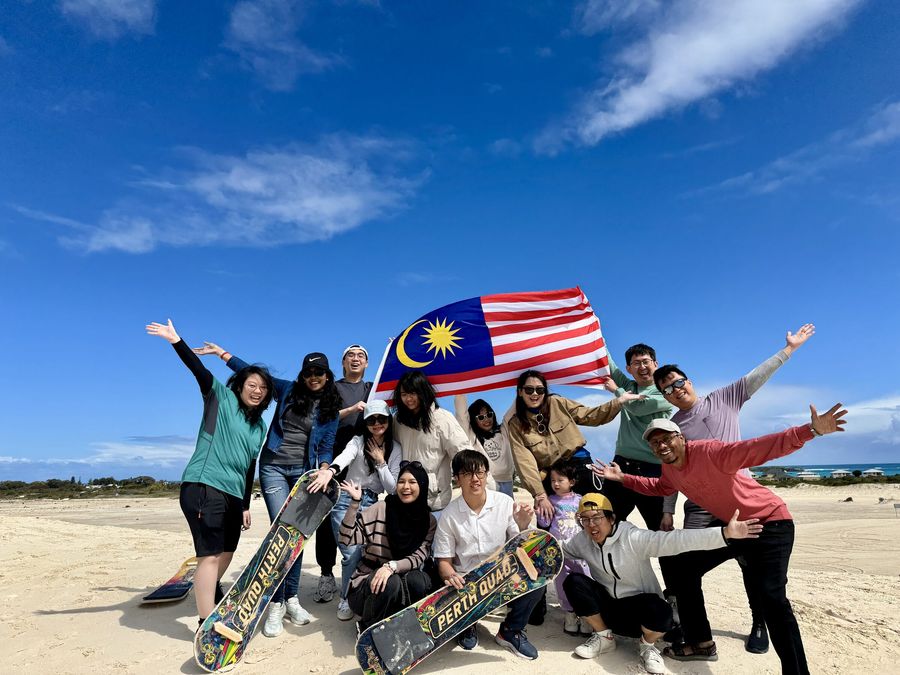 The team waving a Malaysian flag on a beach during a company trip to Perth