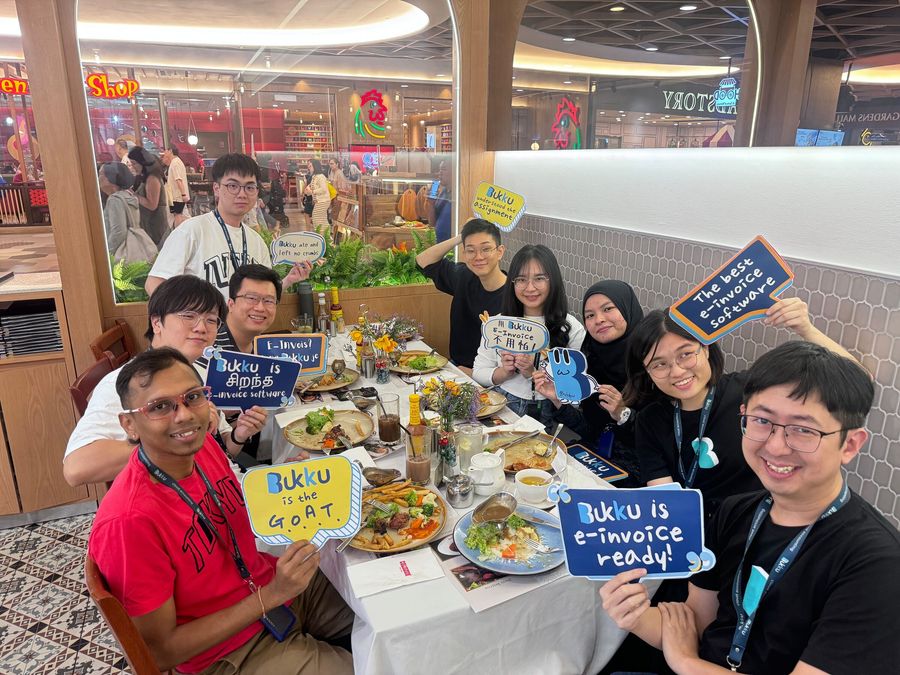 Teammates at a restaurant holding signs that say 'Bukku is e-Invoice ready' to celebrate the MyInvois launch