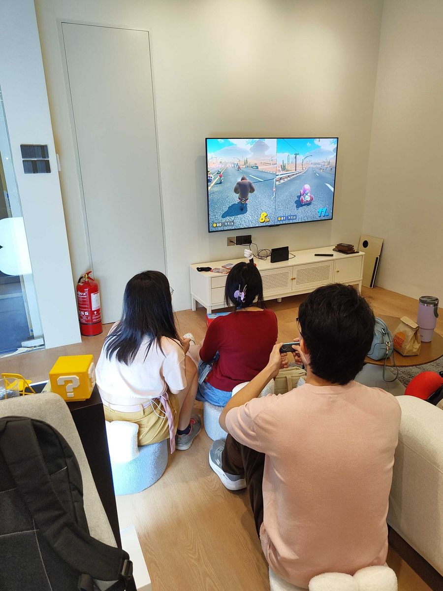 Three teammates playing Mario Kart on the Nintendo Switch 2 in the office lounge